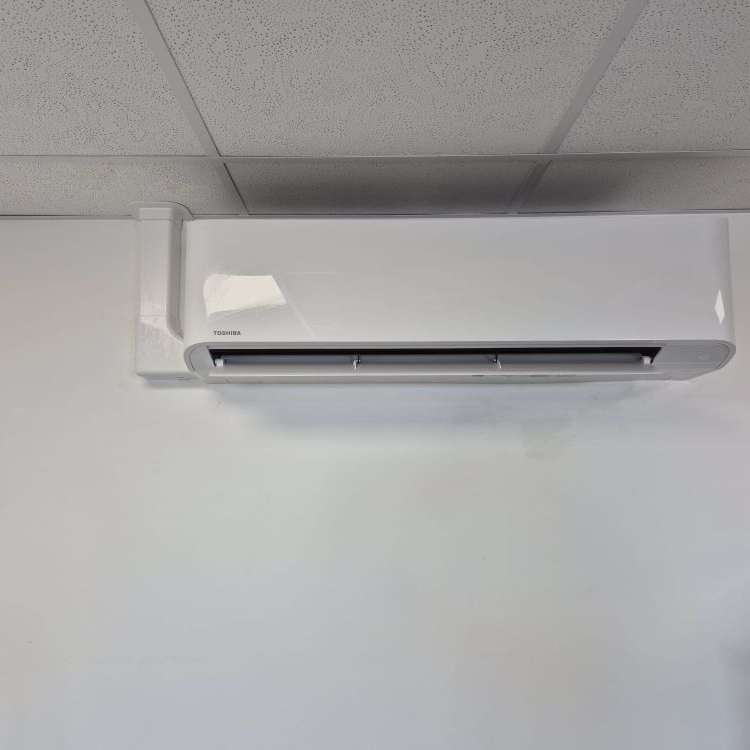 Wall-mounted split air conditioning unit installed in office alongside ducted system